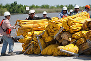 Men in hard hats standing near water next to large pile of bundled large yellow deflated rubber tubing