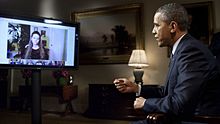 President Barack Obama, seated at right, answers questions about the State of the Union posed by citizens, shown on a flat-screen monitor at left, in the first-ever completely virtual interview from the White House. This interview aired on the official White House Google%2B page on January 30, 2012.