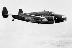 Twin-engined twin-tailed military monoplane in flight, side-on