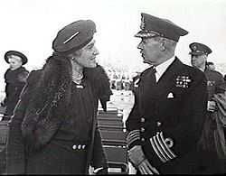 Woman in dark coat and hat talking with man in dark military uniform