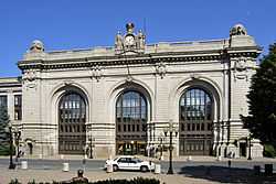 An ornate stone building with three tall arched entrances and a clock in the middle of the top