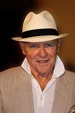 A man wearing a black and white hat including a beige suit and white shirt.