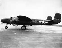 Black and white photo of an early bomber parked perpendicular to camera, facing left. Rearward of the wing is a star in front of horizontal stripes