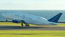 Side view of quadjet lifting above grassy airport against ocean backdrop.