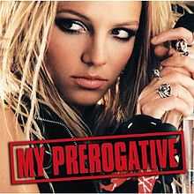 The face of a blonde woman. She is holding a microphone in her hand next to her head, while looking towards the left side of the picture. She is wearing different rings in her fingers. She is wearing a black vest. On the lower part of the image, the words "My Prerogative" are written in red capital letters inside a box of the same color.