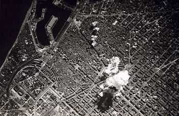 Black-and-white photo of the city from high above. Smoke from a bomb can be seen