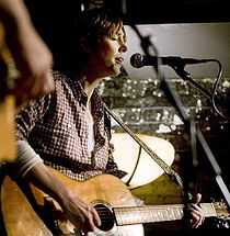 A woman playing guitar and singing into a microphone stand.