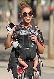 A woman holds her phone in one hand as she walks, a child is attached to her in a harness