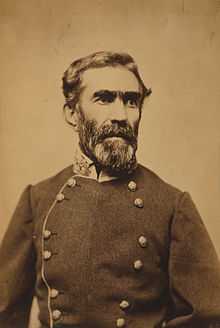 A man with dark wavy hair and a mustache and beard, wearing a military uniform