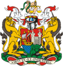 A coat of arms, with a shield showing a sailing ship and a castle with maned lions on either side, surmounted by the helmet from a suit of arms and two hands holding a snake and scales of justice. The motto at the bottom is "Virtute et Industria"