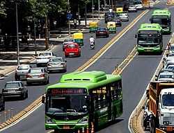 A green coloured Delhi Transport Corporation CNG bus in the middle of the road