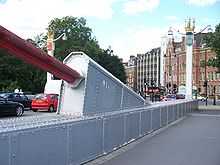 End of a large red suspension cable, attached to a protrusion atop the side of the bridge deck.