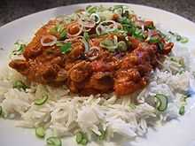 A dish of rice (white) with Kadai chicken (dark orange) on it in a plate