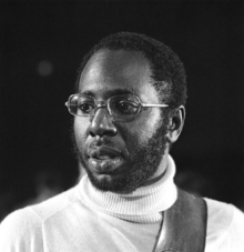 Black and white picture of a man with a beard wearing a turtleneck and glasses.