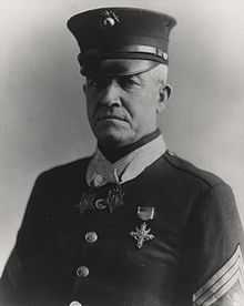 Top half of a serious man in formal 1920s U.S. military dress wearing two star-shaped medals on ribbons around his neck.