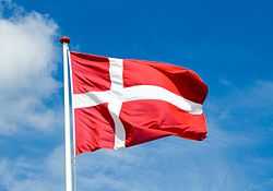 A Danish flag flies from a flagpole against the sky.