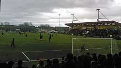 Photograph of players on a football pitch taken from a spectator stand.