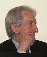 A grey-haired man holding one hand to his face