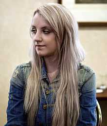 A caucasian female with light blonde hair, wearing a blue short sleeve shirt