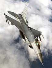 Upright aerial photo of gray jet aircraft flying above clouds.