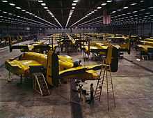 Interior of huge aircraft factory where rows of bombers covered in a yellow layer are manufactured.