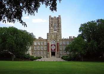 A Gothic style stone building with a central tower in front of a green field with trees on each side.