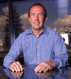 Head and shoulders portrait of smiling 50-year-old man in blue, vertical striped, dress-shirt.