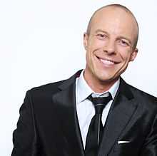 Photograph of a smiling Caucasian man wearing a black suit and tie