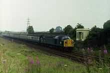 A train on railway tracks in open countryside, passing a large white monument