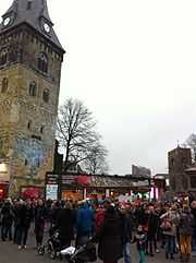 Glass house with many spectators, next to a tall clock tower