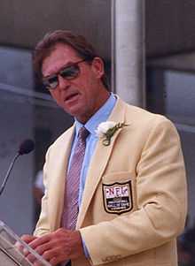 Jack Youngblood, 51-year-old white man dressed in gold jacket, blue shirt, tie and sunglasses, giving his Pro Football Hall of Fame induction speech in 2001.