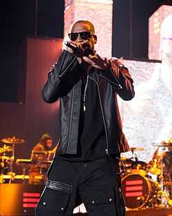 An African-American man wearing sunglasses and a leather jacket raps into a microphone.