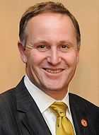 A smiling man wearing a white shirt with a green tie and black jacket