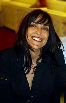 Candid portrait of a 40 year old woman sitting down smiling with shoulder length hair wearing a black blouse.