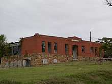 A red brick building with broken windows and lots of vegetation.