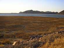 A photo of a dry lakebed with some ruined foundations.