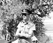 Outdoor half portrait of man in light-coloured military uniform with peaked cap, wearing sunglasses