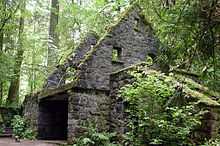  Ruins of a moss-draped stone building rest near a path in a thick forest.