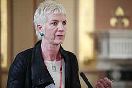 Middle-aged woman with short, very-light hair speaking into a microphone