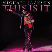 A picture of a man with dark hair pointing with his right hand to his right. The man is wearing a black jacket with a red shirt and black pants. Behind him, there is a black background with the words "MICHAEL JACKSON" in white print and, underneath it, "THIS IS IT" written in pink.