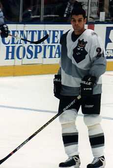 hockey player in white jersey holding hockey stick.