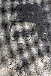 A man in spectacles and a songkok, looking left