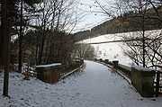 A snow-covered scene, lit by low sunlight, shows the footpath curving to the left before disappearing behind bare trees