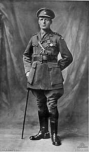 A full length portrait of a man in military uniform wearing two military medals and leaning on a swagger stick.