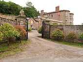 A red-brick, three-storey, historic house with a red-brick wall and gates in front