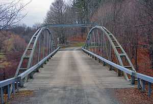 A metal bridge with two forked arches on the side and tie rods holding the middle together, seen from one end