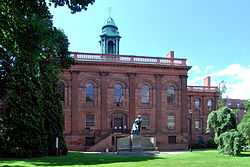 An ornate three-story brick building with a pedimented front section and tall gray cupola.