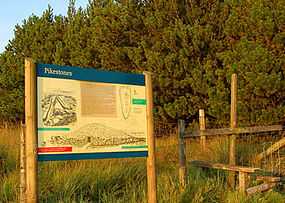 a large sign at the edge of a field with trees and a wooden fence on the left side