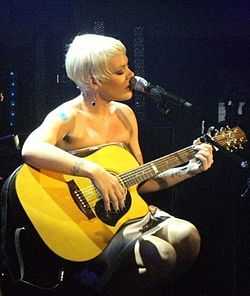 A woman with short blonde hair singing with her microphone while playing a guiar