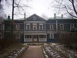 A blue two-story house with white trim and many windows, surrounded by birch trees.